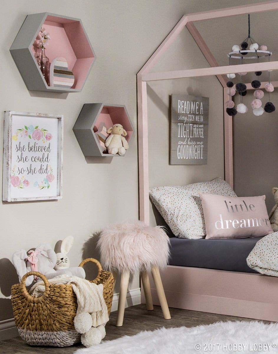 دکوراسیون پاستلی اتاق کودک دختر که تخت سایباندار صورتی، قفسه های دکوری خاکستری، تابلوهای انگیزشی و آویز بالا تخت دارد
